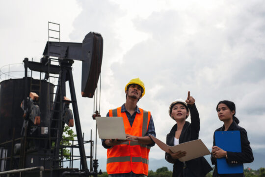 engineering-team-stands-beside-working-oil-pumps-with-sky engineering-team-stands-beside-working-oil-pumps-with-sky